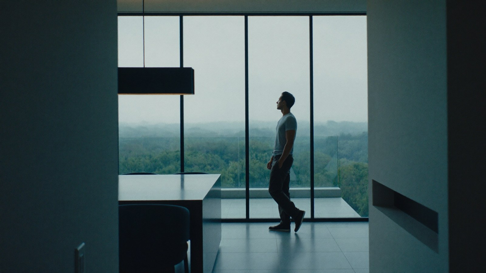 A composed, confident man at ease by a window in a modern interior, fully dressed